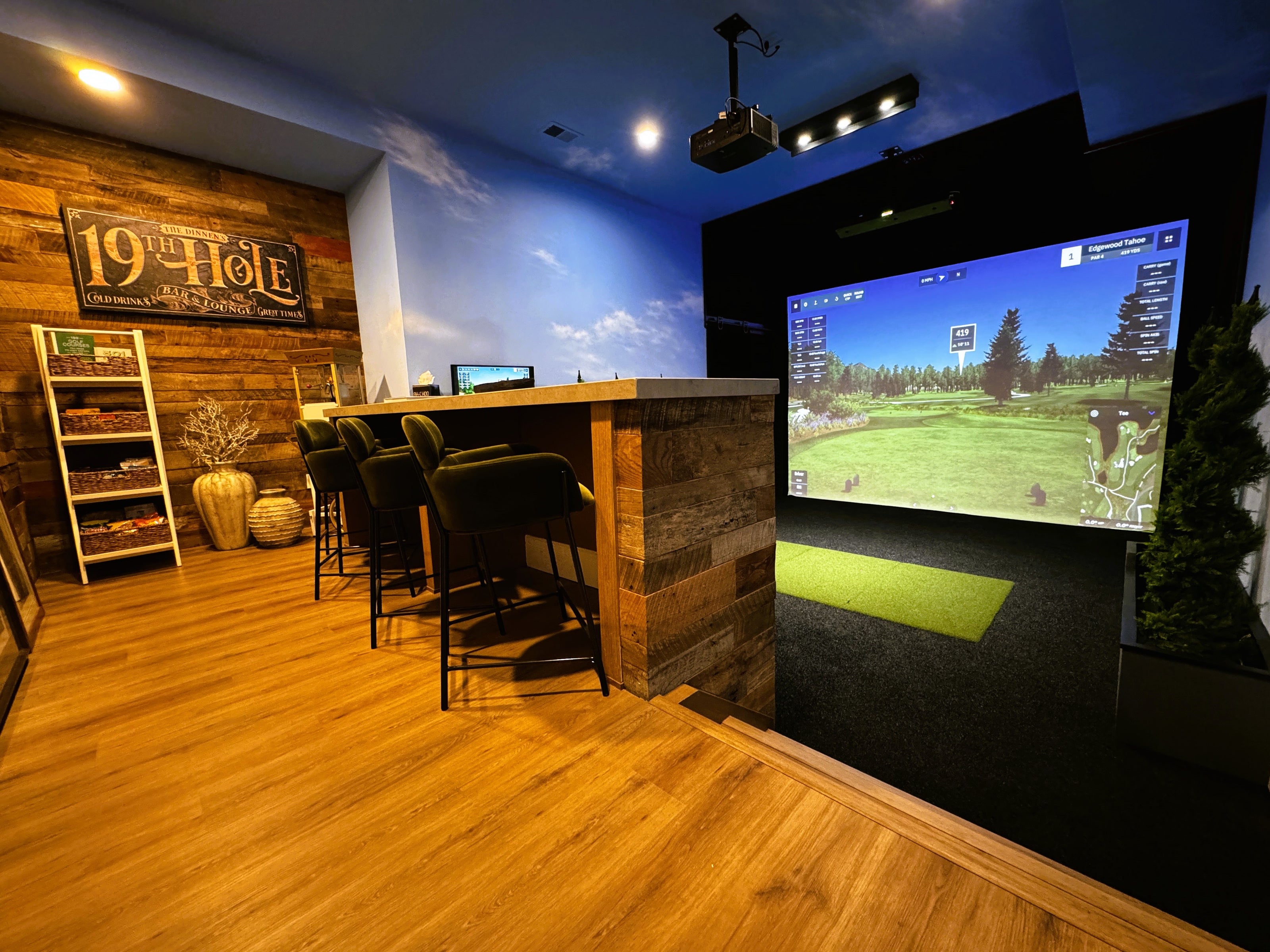 A home golf simulator with blue sky walls and wood bar area.