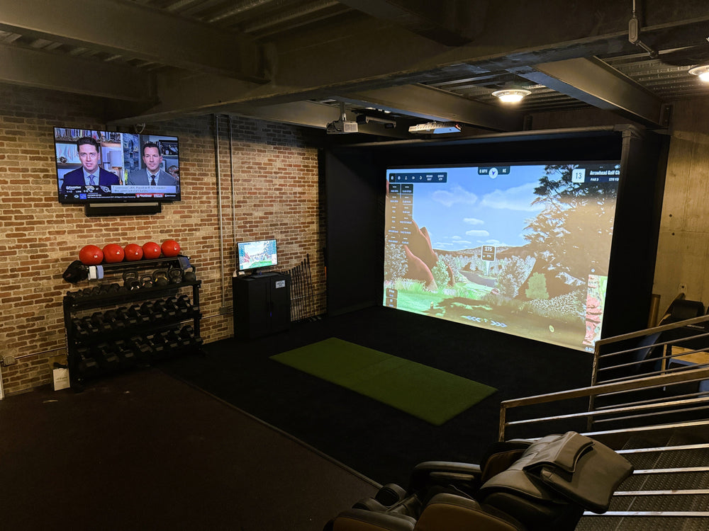 A golf simulator and gym area with brick wall with a tv.