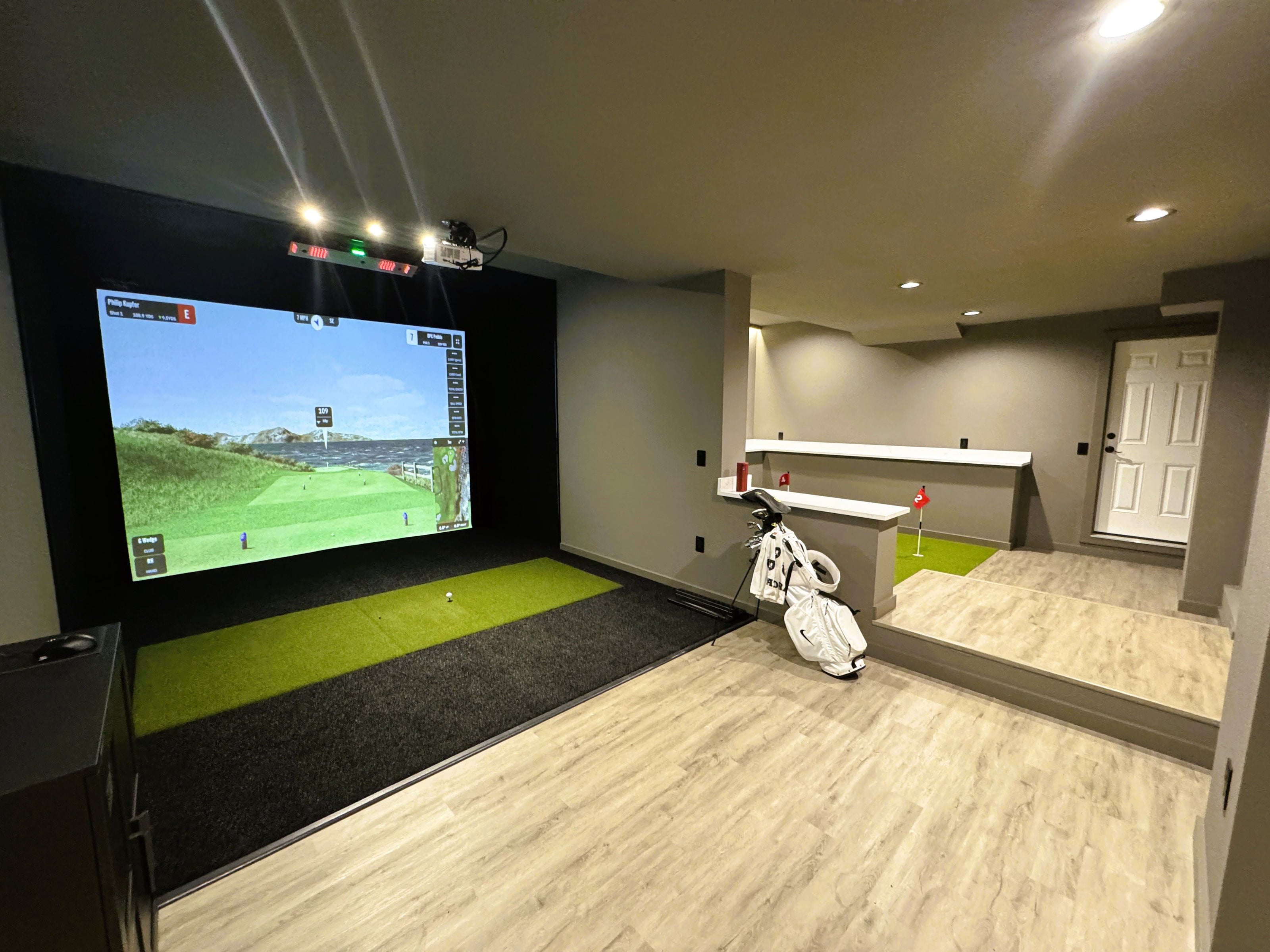 Basement area featuring a home golf simulator and a putting green with four holes.