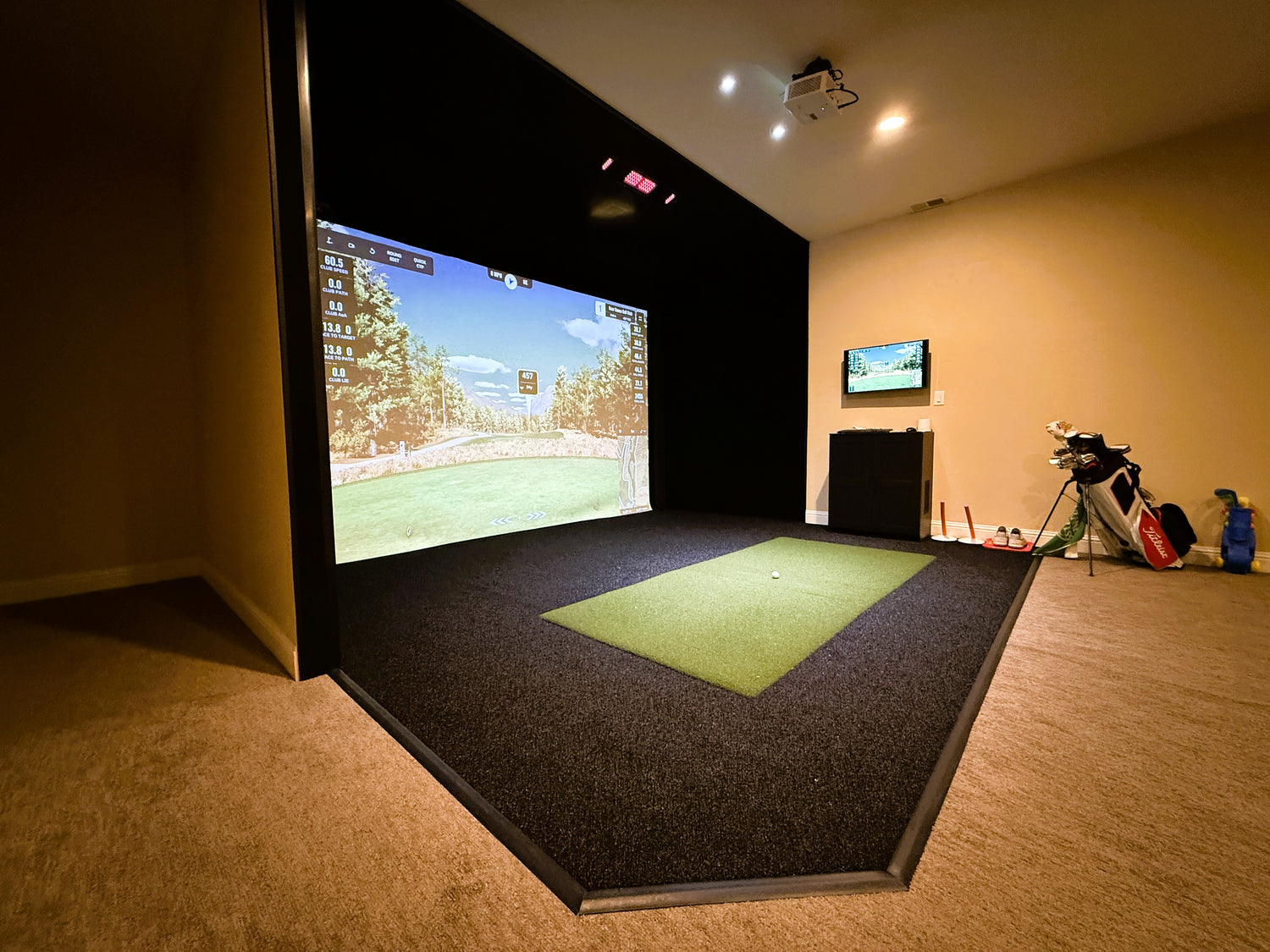 Golf simulator setup in a room with a screen displaying a golf course.