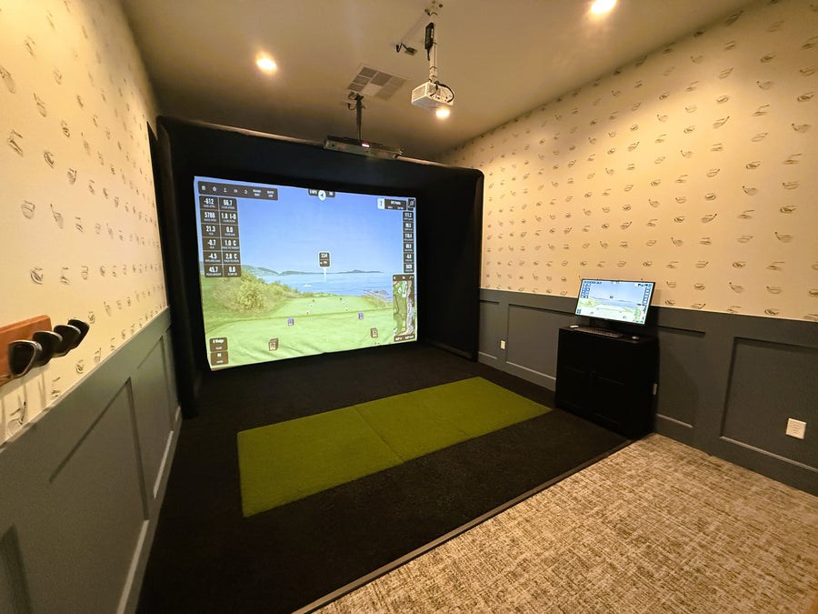 Golf simulator setup in a room with a large screen and computer.