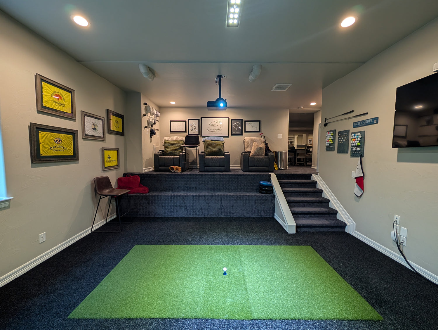 Indoor golf simulator setup in a home entertainment room with green turf and various decor elements.