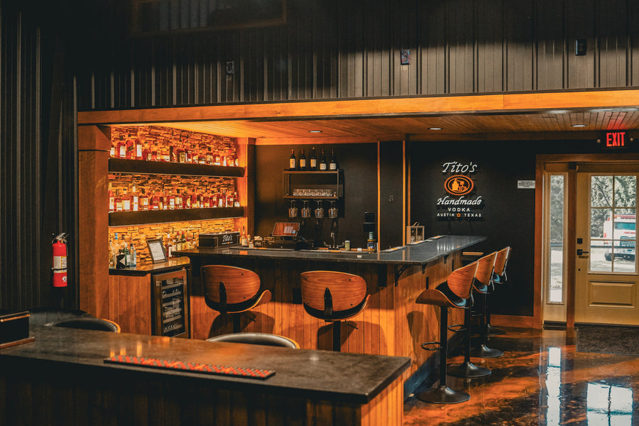 Bar area with wooden furniture and shelves stocked with bottles, featuring a Tito's sign.