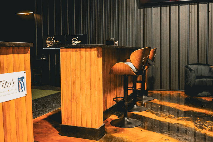 Wooden bar counter with stools in a dimly lit room, featuring 'Tito's' branding.