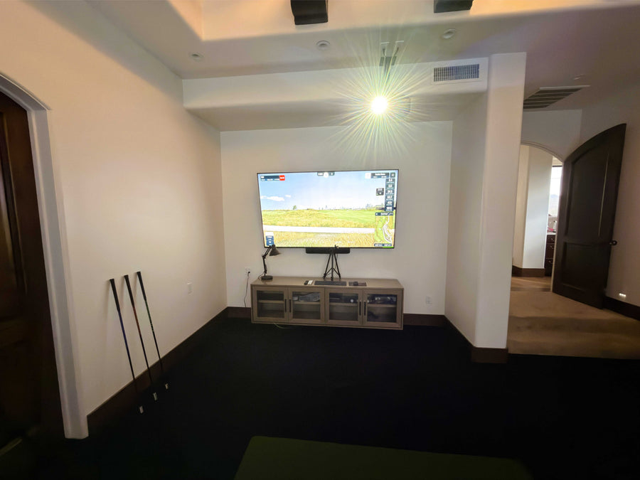 Golf simulator room with a TV mounted on the wall displaying a sports game.