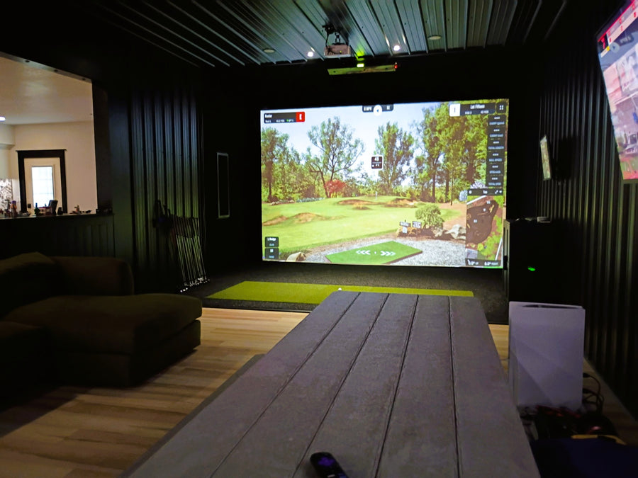 Indoor golf simulator setup in a room with a screen displaying a golf course.
