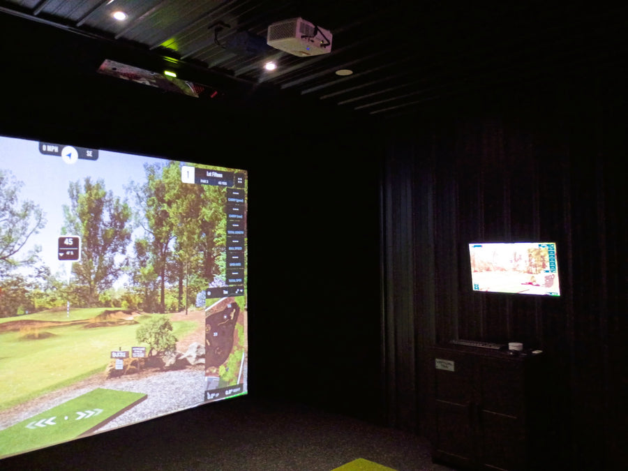 Golf simulator setup with large screen and smaller monitor in a dark room