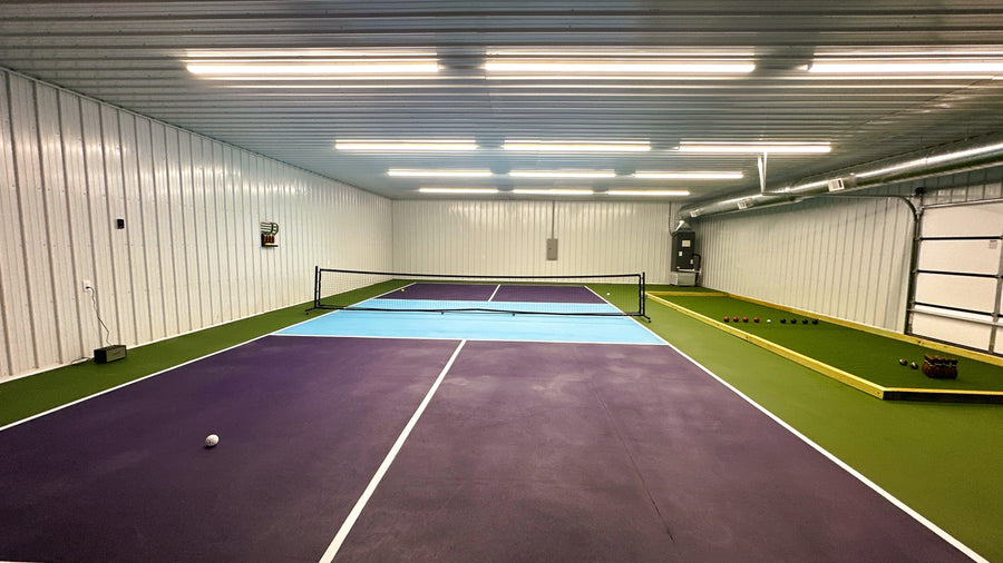 Indoor tennis court with purple and blue surface, white lines, and a net. With indoor golf simulator.