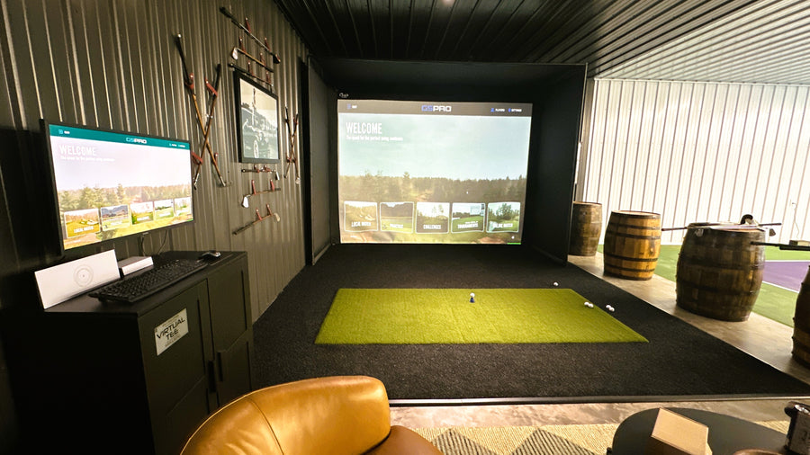 Indoor golf simulator setup with two screens displaying golf courses.