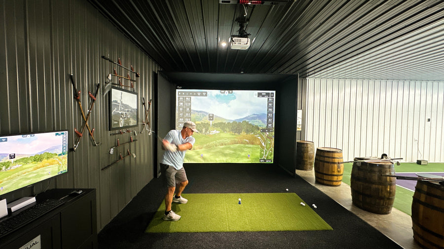 Man playing golf in a home simulator setup with multiple screens and equipment.