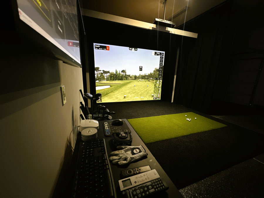 Golf simulator setup with screen displaying a golf course, controls, and a green mat.