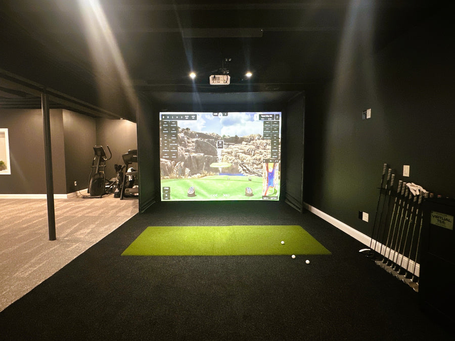 Indoor golf simulator setup with screen displaying a golf course and golf clubs on the side.