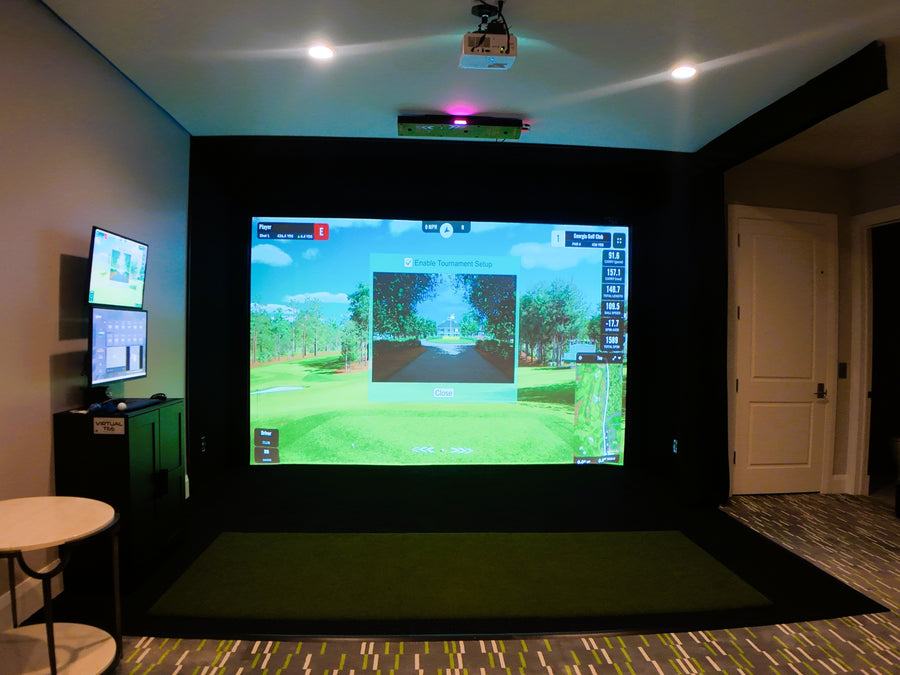 Indoor golf simulator setup with projection screen and multiple monitors in a room.