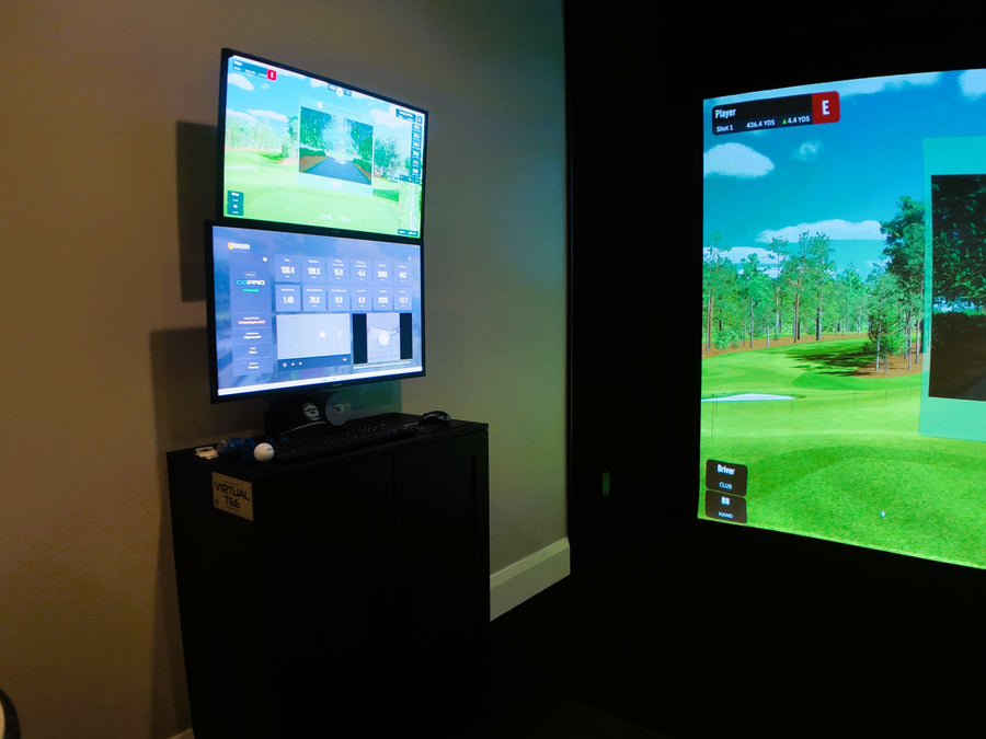 Two screens displaying a golf simulation game in an indoor golf simulator room setting.