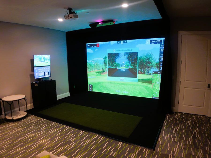 Indoor golf simulator setup with projection screen and multiple monitors in a room.