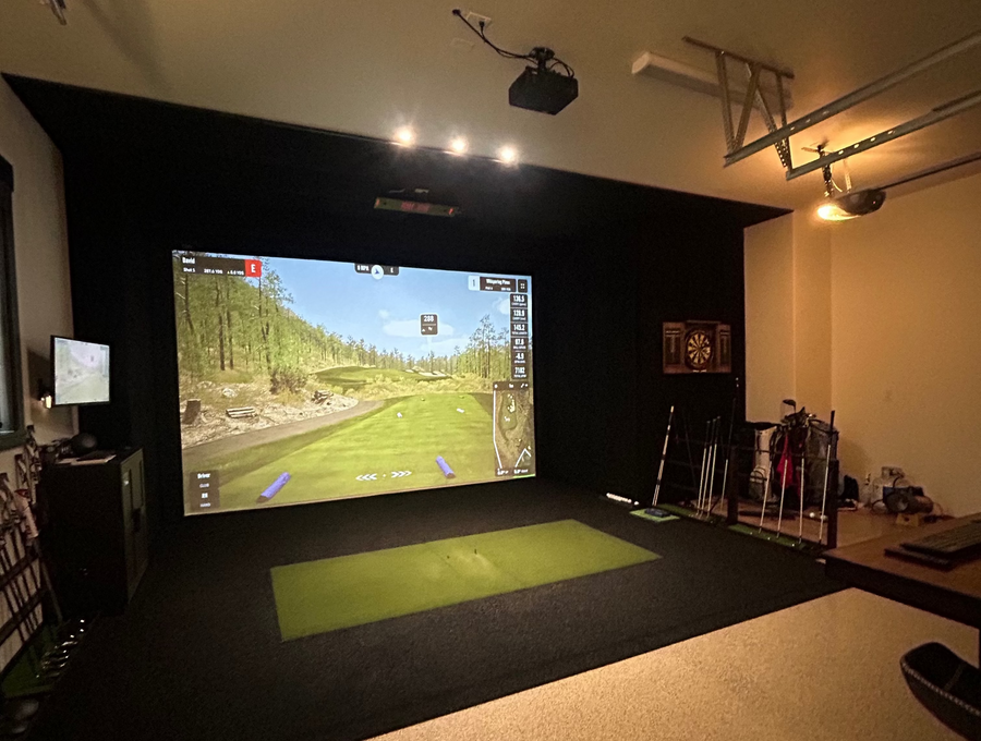 Indoor golf simulator setup in a room with a large screen displaying a golf course.