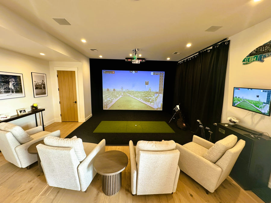 Indoor golf simulator setup with a large screen displaying a sports game, surrounded by comfortable seating and additional screens.