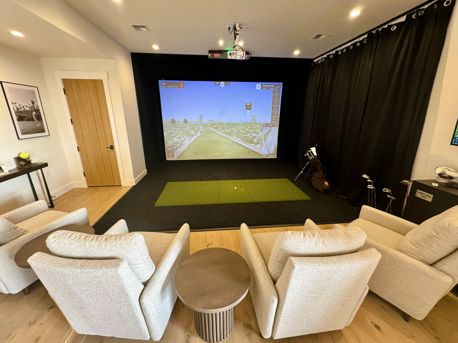 Indoor golf simulator with a screen displaying a video game, surrounded by comfortable seating.