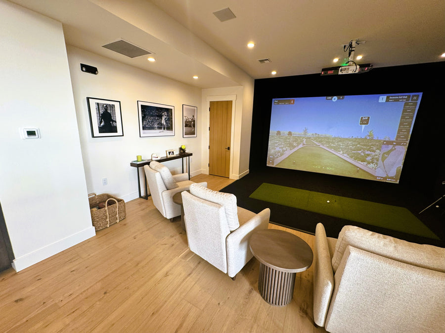 Indoor golf simulator setup with large screen displaying a sports game, surrounded by comfortable seating.