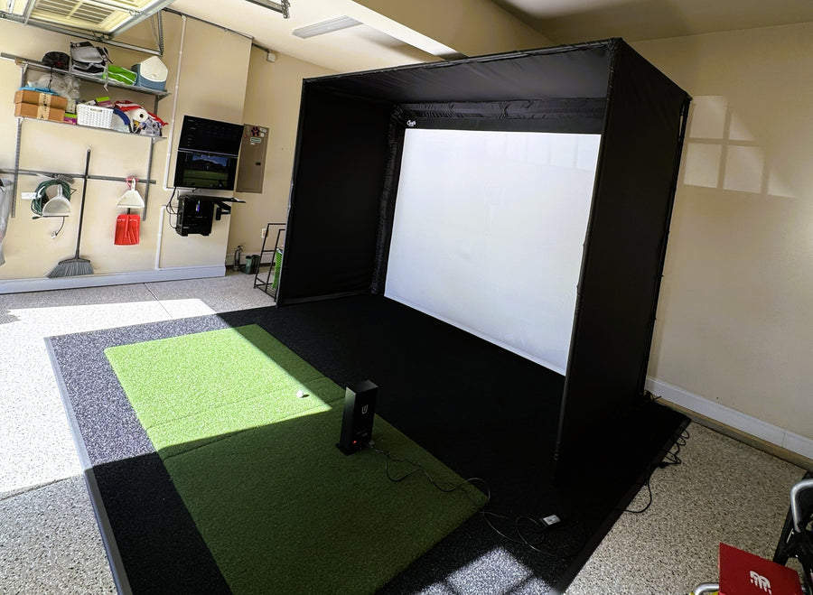 Golf simulator setup in a home garage with projection screen and equipment.