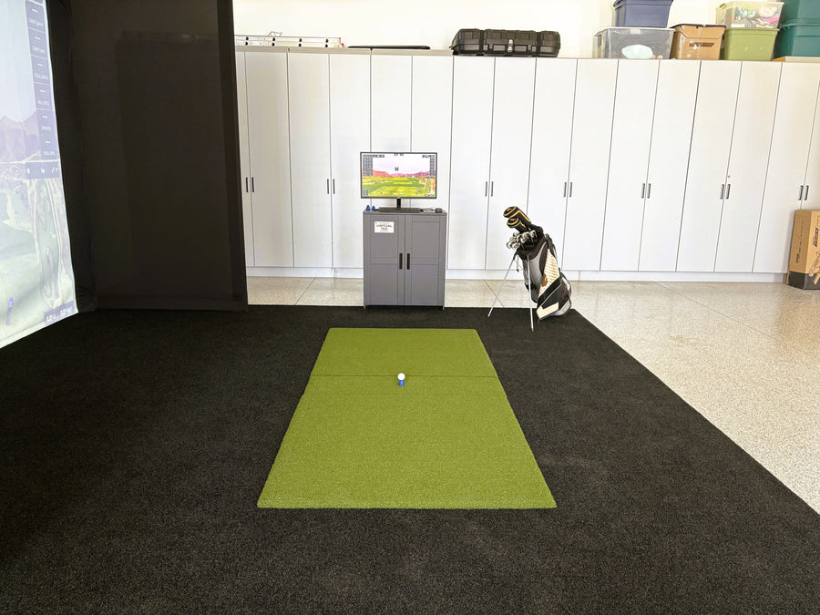 Golf simulator setup in a room with a green mat and TV screen.
