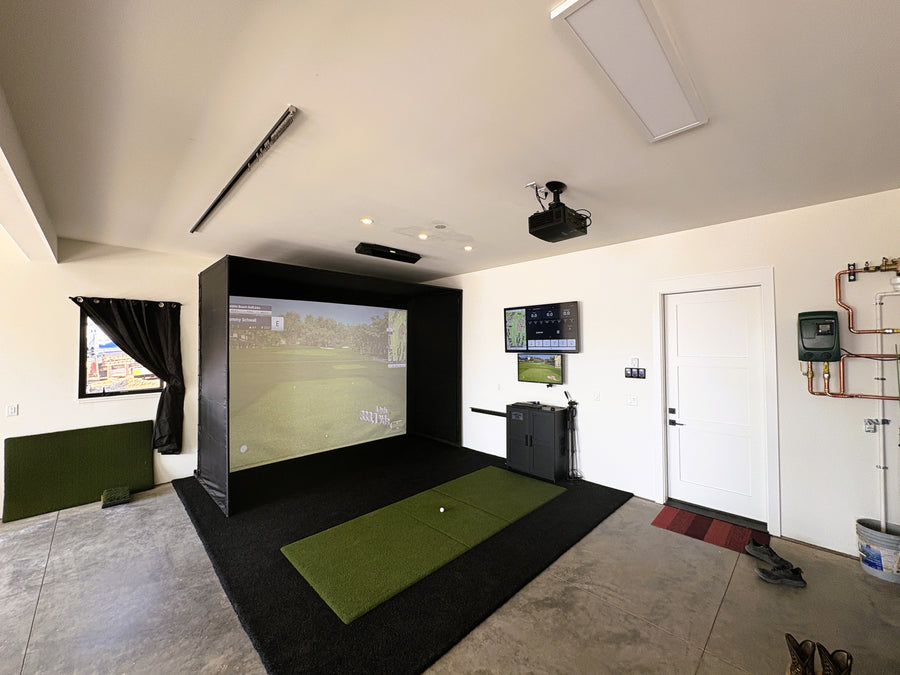 Indoor golf simulator setup with screen, projector, and golf mat in a room.