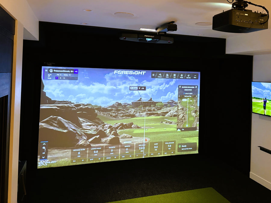Golf simulator setup with screen displaying a golf game on a wall.