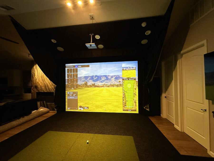 Indoor golf simulator setup in a room with a screen displaying a golf course.