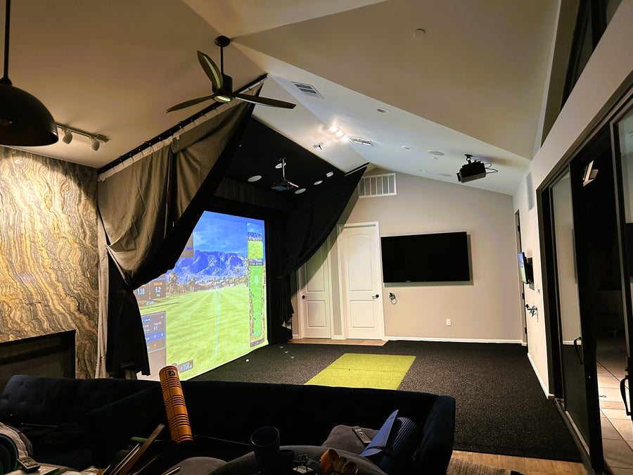 Home golf simulator setup with a large screen displaying a game, surrounded by comfortable seating and decorative elements.