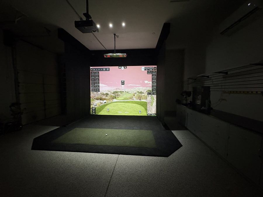 Indoor golf simulator room with screen displaying a golf course.