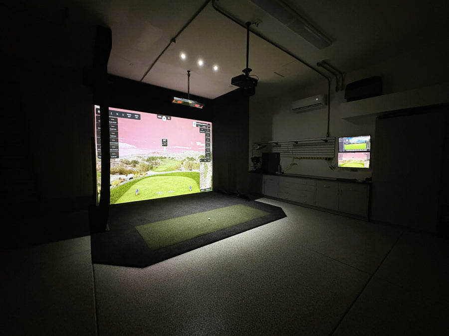 Indoor golf simulator setup in a dark room with two screens displaying golf courses.