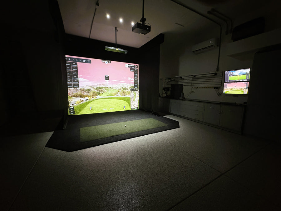 Golf simulator setup in a dark room with screens displaying a golf course.
