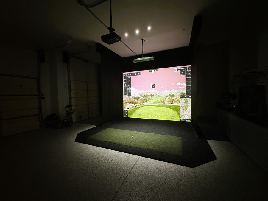 Indoor golf simulator setup in a garage with a screen displaying a golf course.
