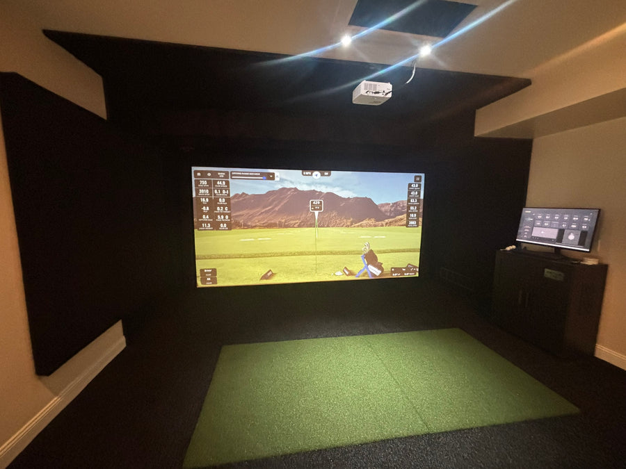Golf simulator setup with screen displaying a golf course and control panel on a wall.