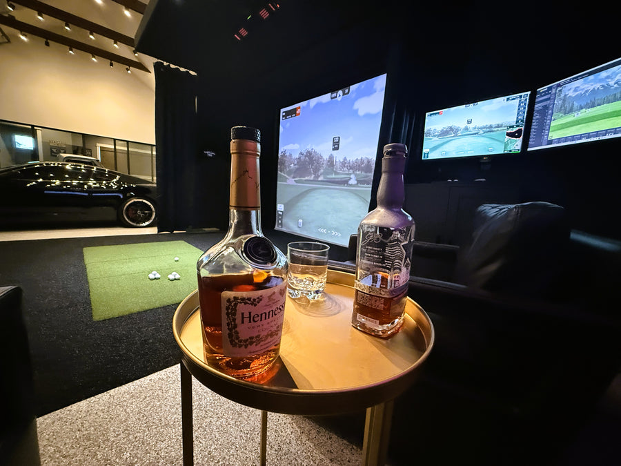 Two Hennessy bottles on a table in a golf simulator space.