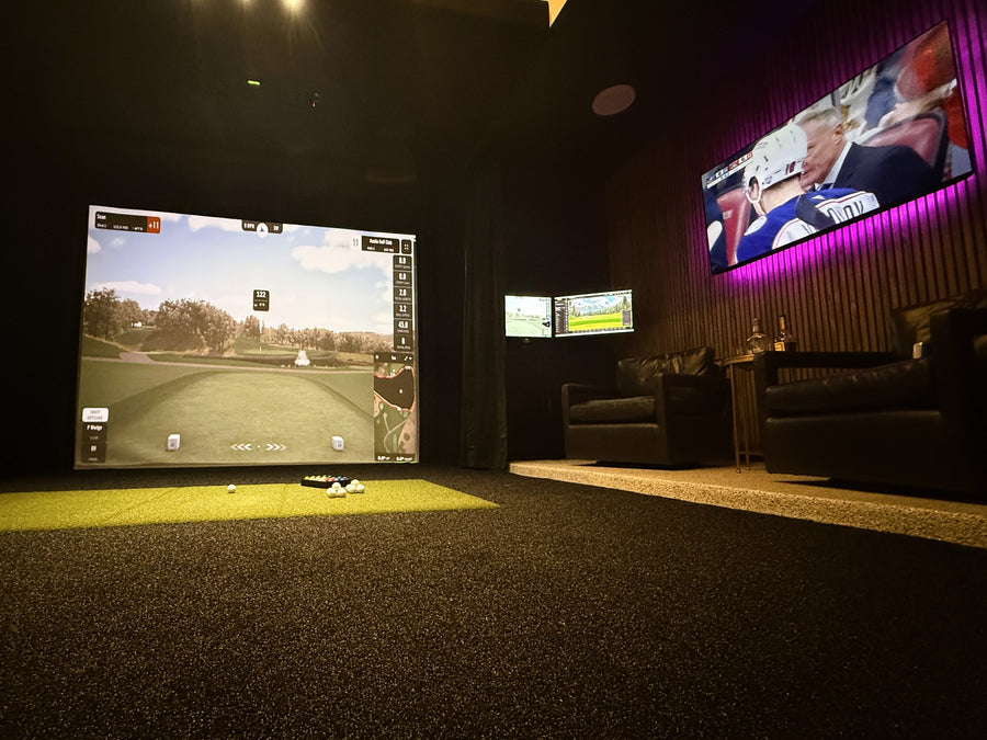 Golf simulator setup with two screens displaying different content, surrounded by dark walls.