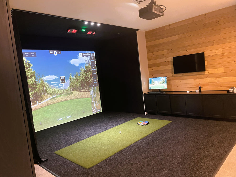 Indoor golf simulator setup with screen displaying a golf course and wooden wall.