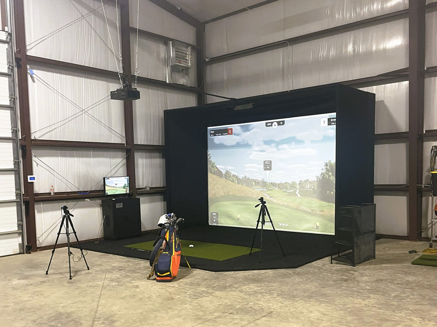 Indoor golf simulator setup with screen displaying a golf course, golf bag, and equipment.