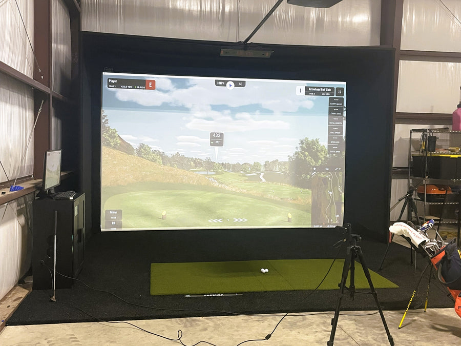 Golf simulator setup with screen displaying a golf course and equipment on a stand.