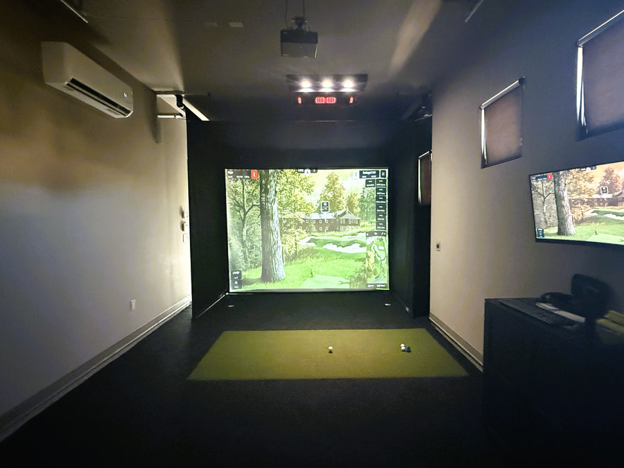 Indoor golf simulator setup with screens and projection on a wall.
