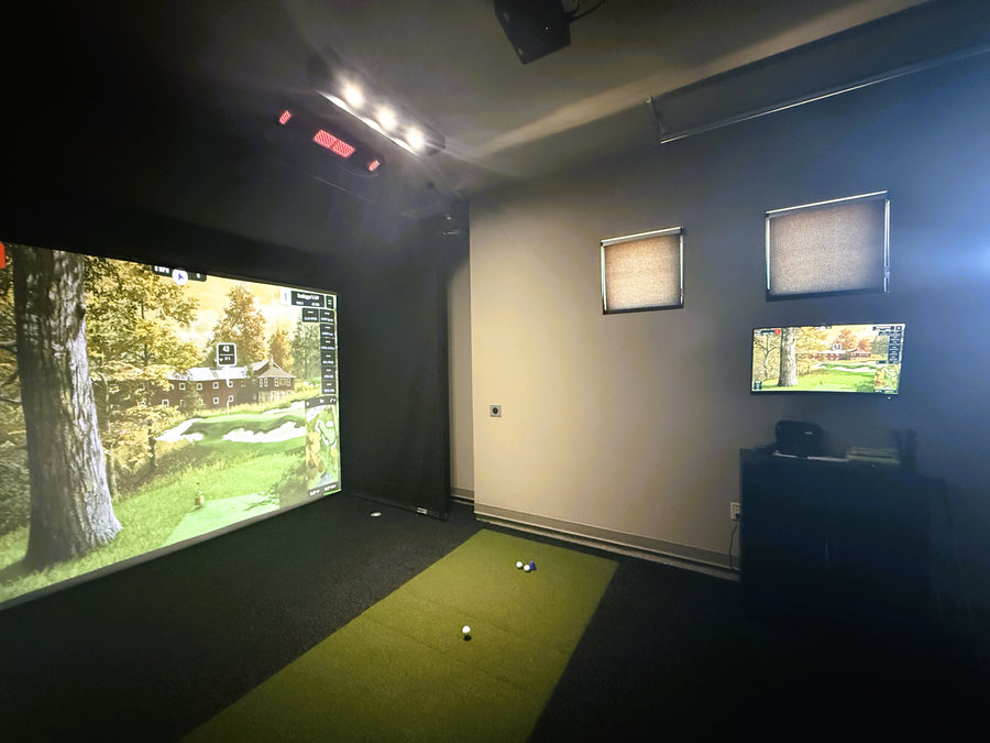 Golf simulator room with screen displaying a golf course and additional screens on the wall.