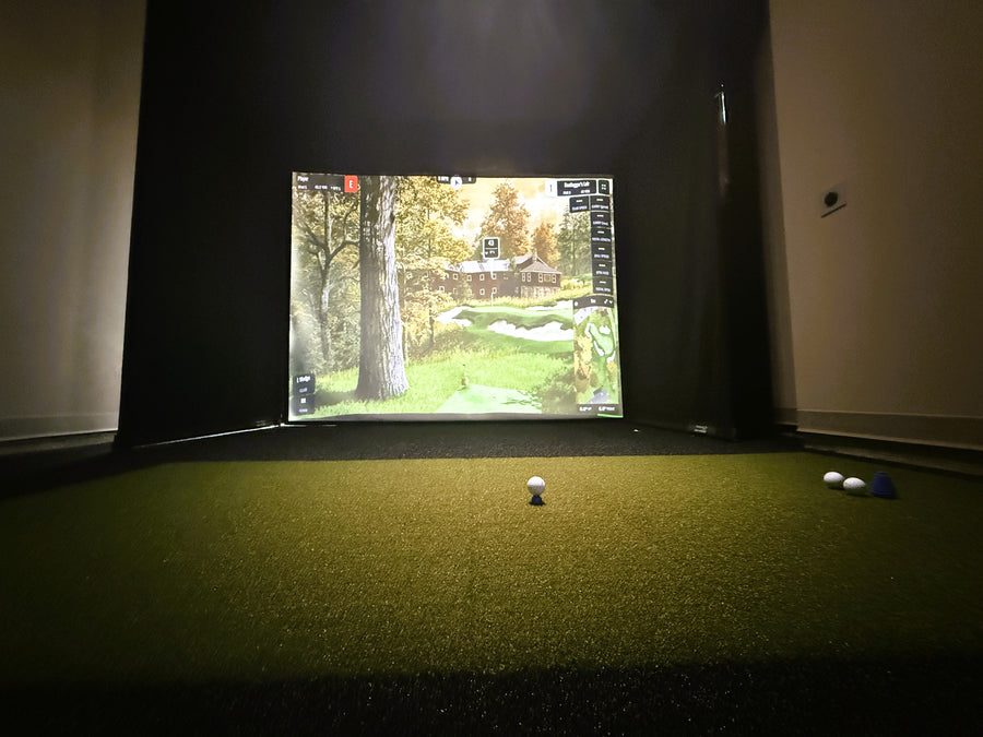 Golf simulator setup with screen displaying a golf course and golf balls on a green surface.