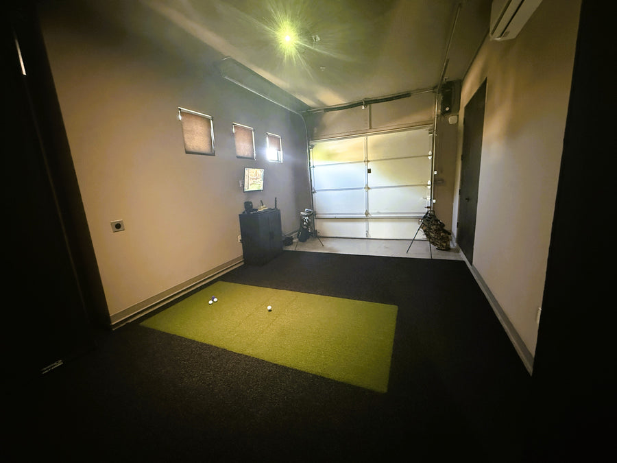 Indoor golf simulator setup with green mat and equipment in a room.