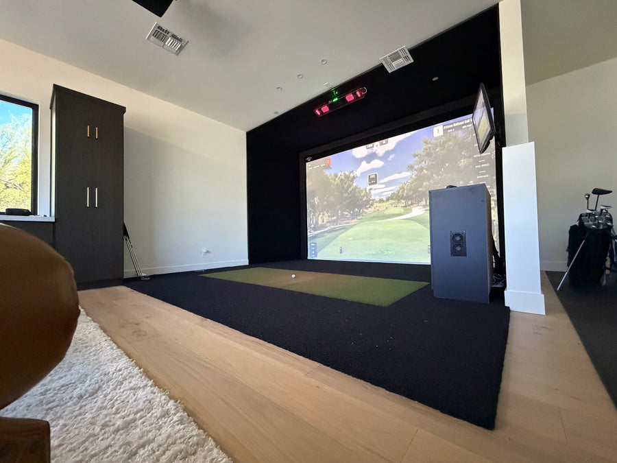 Indoor golf simulator setup in a room with a screen displaying a golf course.