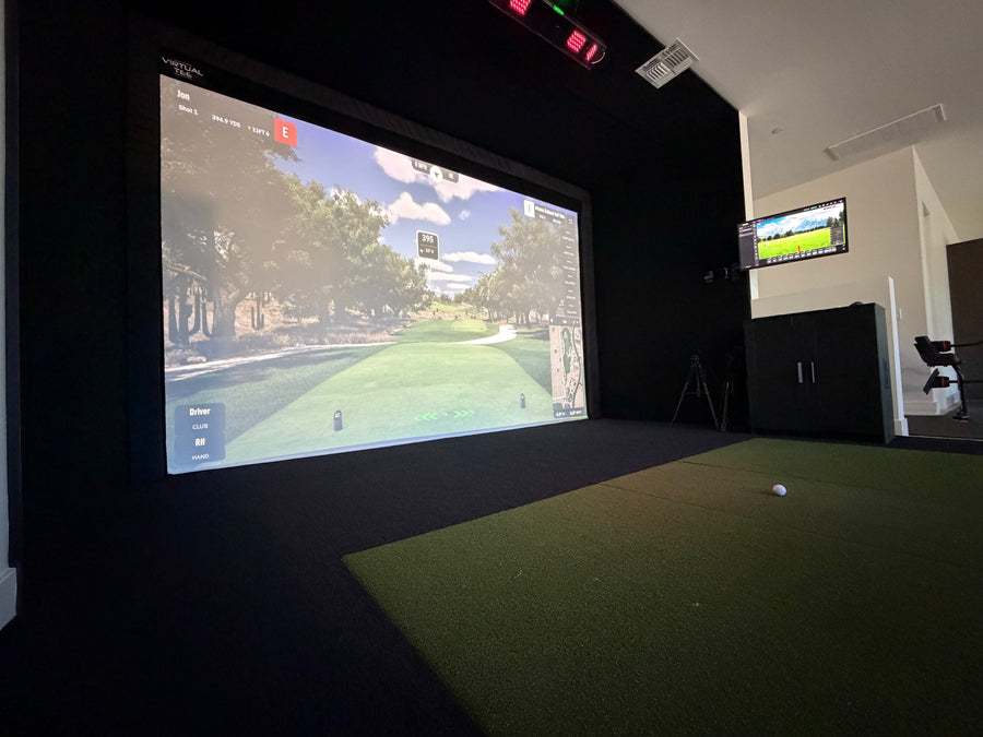 Golf simulator setup with screen displaying a golf course and ball on a green floor.