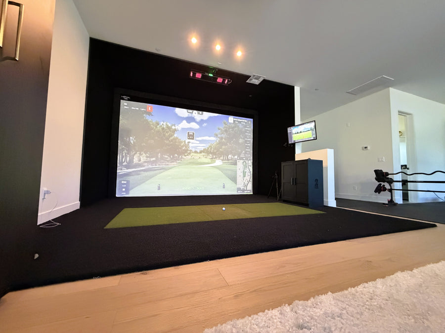 Indoor golf simulator setup in a modern room with a screen displaying a golf course.