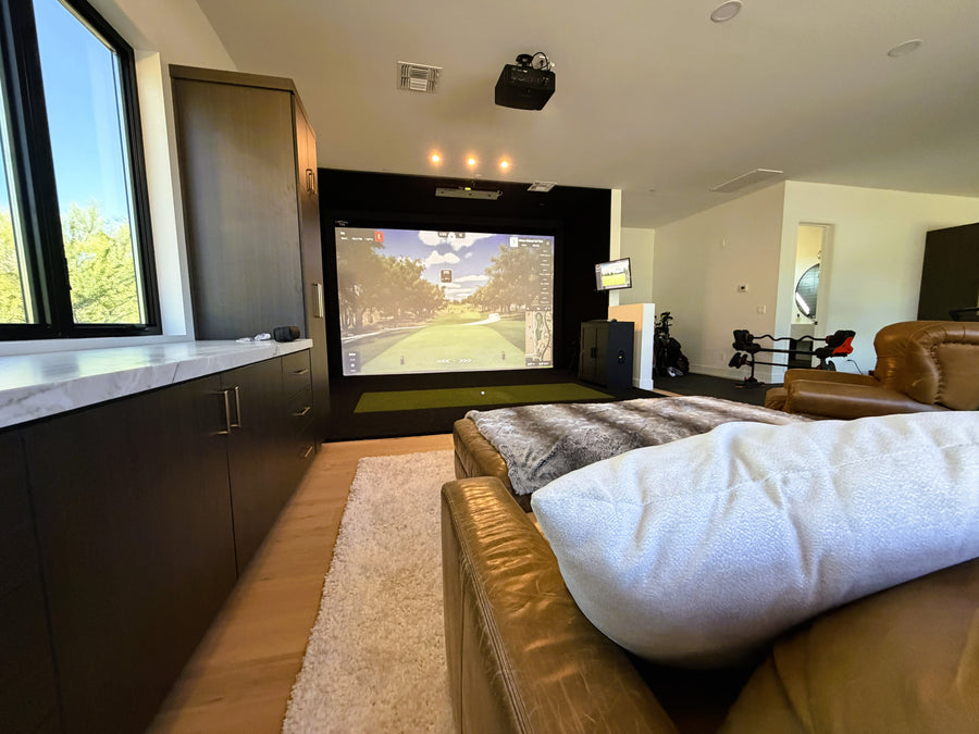 Modern living room with a large golf simulator screen displaying a golf course, surrounded by furniture.