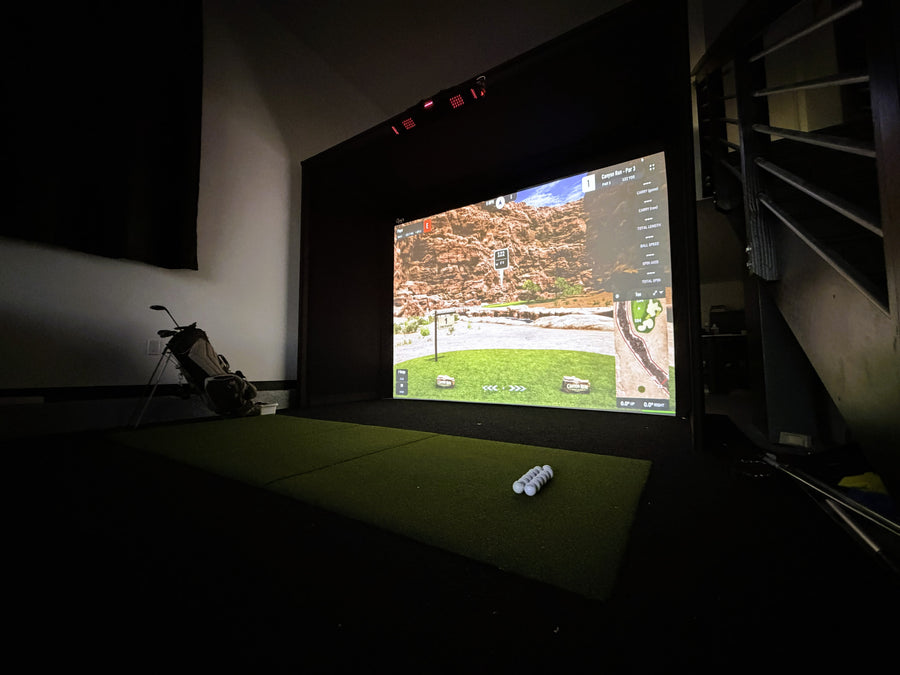 Indoor golf simulator setup with screen displaying a golf course.