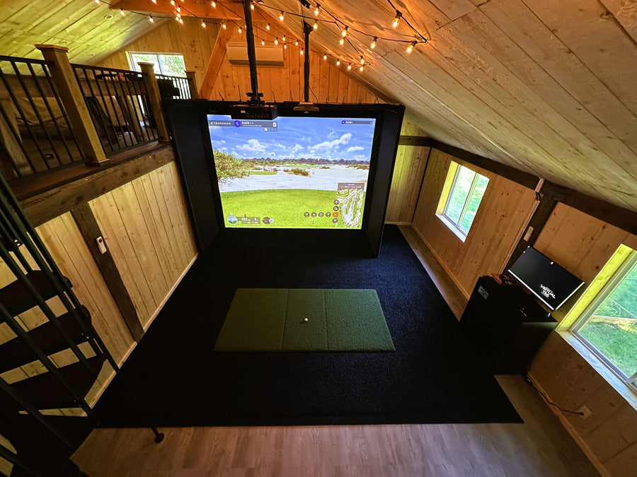 Indoor golf simulator setup in a room with wooden walls and a large screen displaying a golf course.