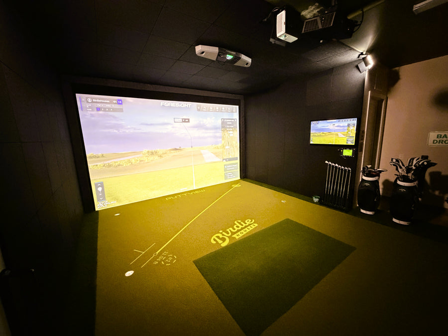 Indoor golf simulator setup with projection screen and golf equipment.